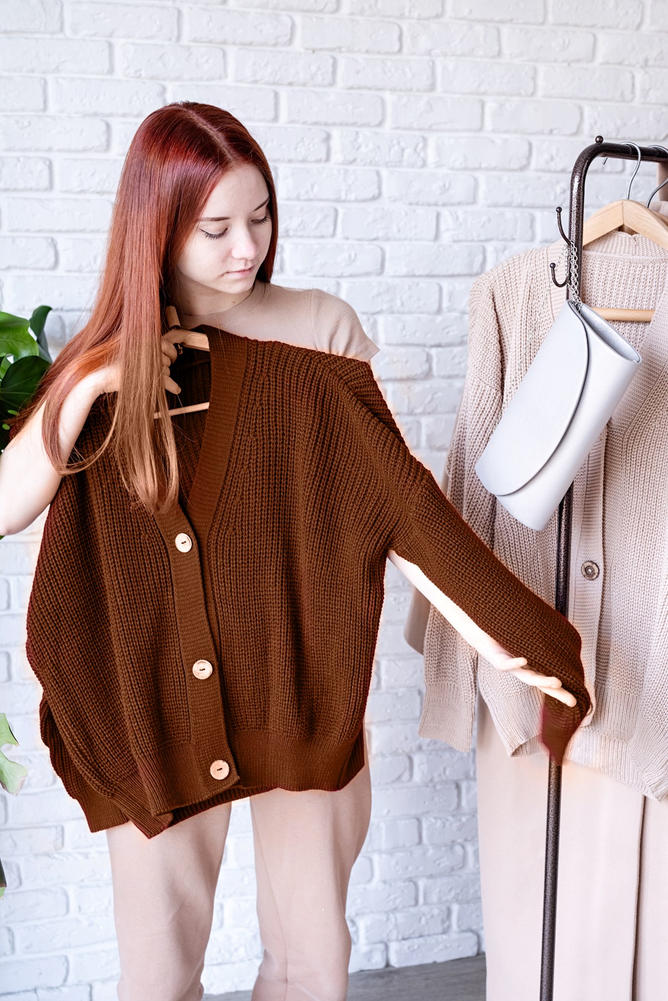 Mocha Mousse - color of the year 2025. beautiful young woman in trendy outfit standing in front of hanger rack and choosing outfit dressing. Selection of a wardrobe, stylist, shopping